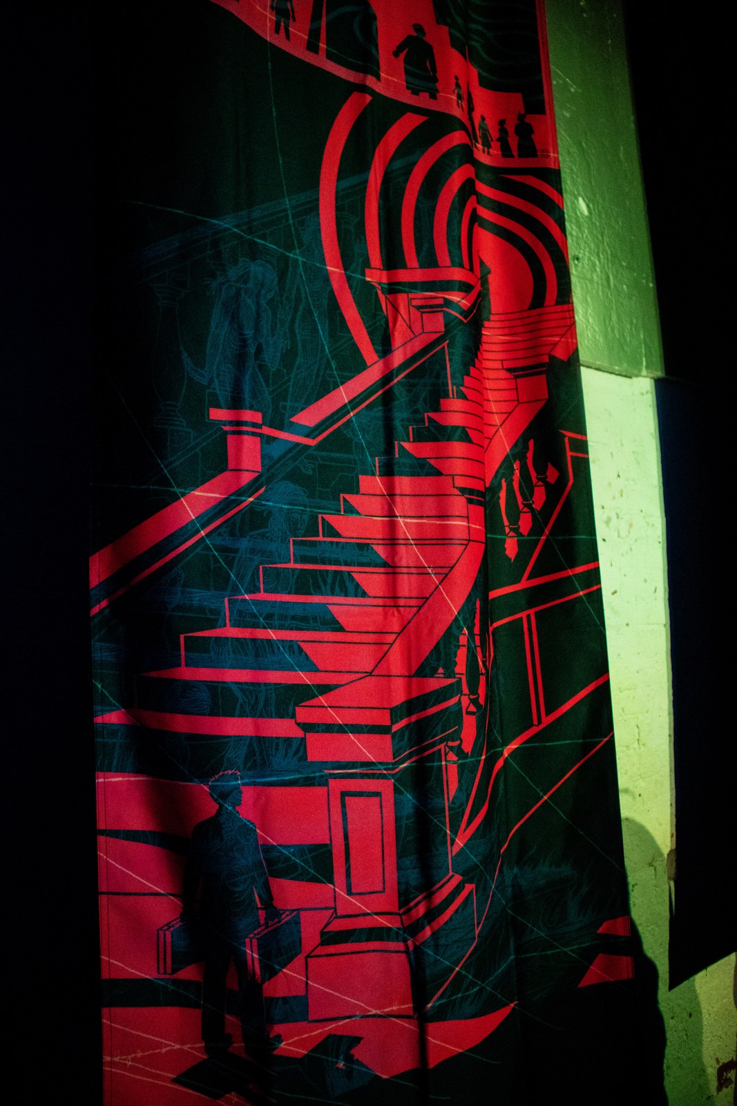 An Ivor's Compass banner hanging at Stanley Arts — a figure with suitcases climbing a red staircase through a crowd of Windrush arrivals, coloured light striking the wall