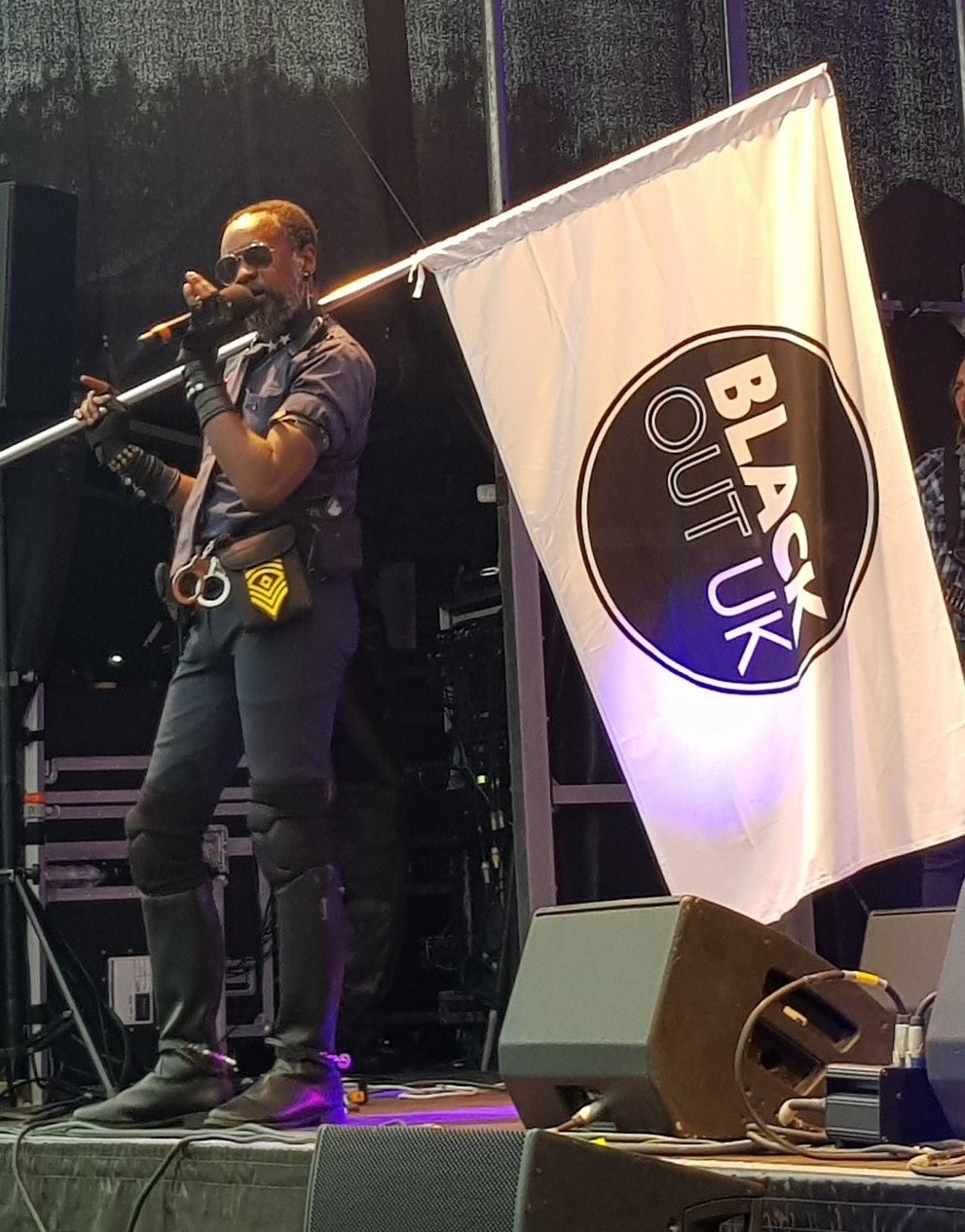 David McAlmont sings on stage beside the BLACK OUT UK flag at Croydon Pride