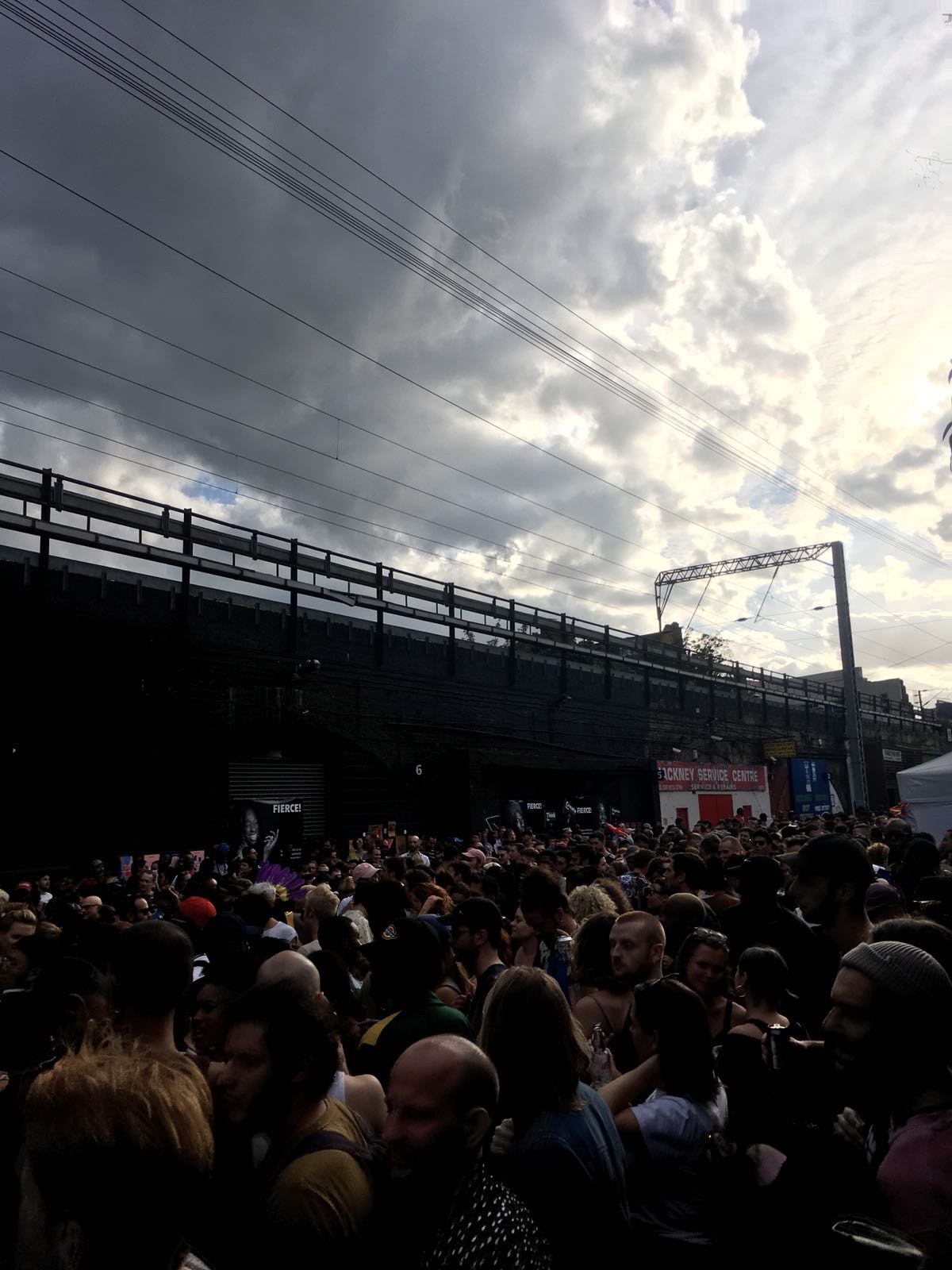 A large crowd gathered under a railway bridge near a FIERCE! stage banner at Hackney Carnival