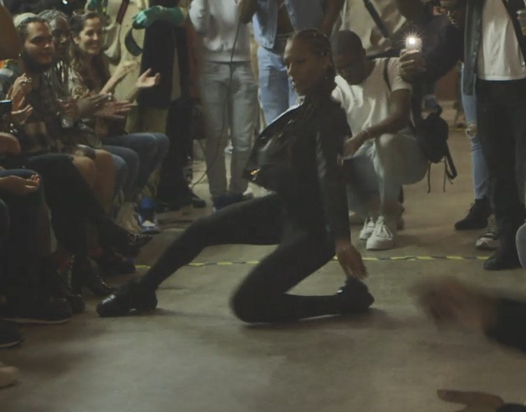 A dancer drops low mid-vogue between rows of audience, phone lights up, at the Pearl's Return ball