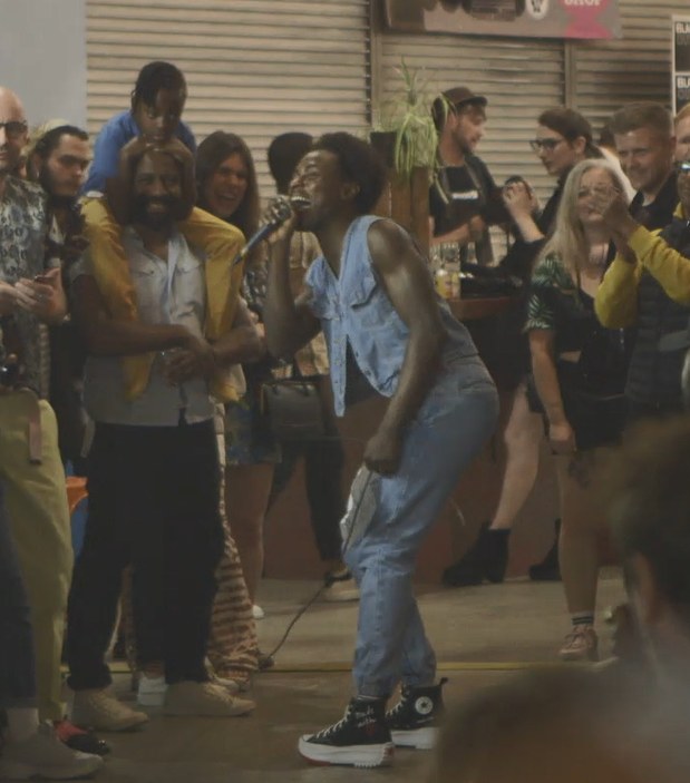 A singer in double denim performs to a delighted crowd in a Brixton Market aisle